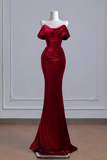 A floor-length off-the-shoulder evening gown in deep burgundy velvet, displayed on a white mannequin against a light gray paneled wall.