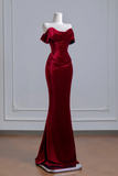 A floor-length off-the-shoulder evening gown in deep burgundy velvet, displayed on a white mannequin against a light gray paneled wall.