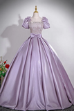 A lavender purple ball gown with a beaded bodice, puff sleeves, and a large bow at the waist, displayed on a mannequin against a light gray background.