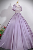 A lavender purple ball gown with a sparkling beaded bodice, puffed short sleeves, and a large bow at the waist, displayed on a mannequin.