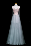 A strapless formal gown displayed on a mannequin against a black background. The dress features a fitted bodice with rose gold sequins and a long, flowing pale blue tulle skirt with a matching sheer veil.