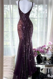 A floor-length, sleeveless evening gown with a deep V-neckline and spaghetti straps, covered in shimmering vertical sequins. The dress is displayed on a white mannequin in a bright room with sheer white curtains, a window view, and a side table with pink flowers.