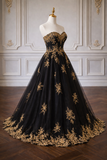 Black evening gown with gold embroidery on a mannequin against a decorative wall.