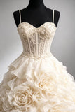 An ivory strapless ball gown with a heavily embellished lace corset bodice and a voluminous ruffled skirt featuring large fabric roses, displayed on a black mannequin torso against a neutral gray background.