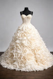 An ivory ball gown wedding dress with a structured corset bodice and a voluminous skirt made of layered fabric roses, displayed on a black mannequin against a gray studio background.