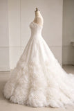 A voluminous white wedding gown with 3D floral rosettes and a strapless sweetheart neckline, displayed on a mannequin in a bright, minimalist room.