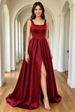 A woman models a floor-length burgundy satin gown with a square neckline, fitted bodice, and high thigh slit, standing in a bright white arched hallway with wood floors.