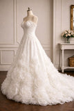 A strapless white wedding gown with a sweetheart neckline, fitted lace bodice, and a voluminous skirt made of layered rosette flowers, displayed on a mannequin in an elegant indoor room.