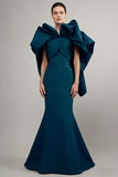 Woman wearing a teal evening gown with a large bow on a gray background