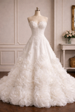 A strapless white wedding gown with a sweetheart neckline, fitted lace bodice, and a voluminous skirt made of layered rosette flowers, displayed on a mannequin in an elegant indoor room.