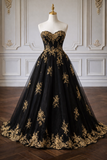 Black evening gown with gold embroidery on a mannequin against a decorative wall.